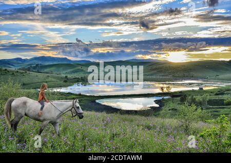 Une petite fille se promette sur un cheval blanc en montagne au coucher du soleil Banque D'Images