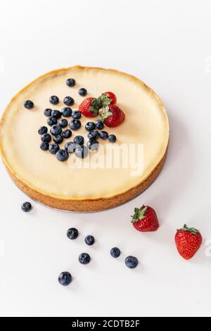 Cheesecake entier avec fraises fraîches et bleuets sur une table blanche. Banque D'Images