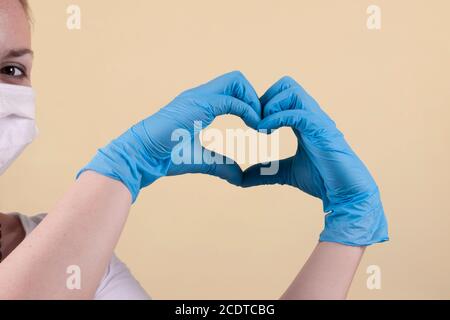 Le médecin montre un coeur en repliant ses doigts. Les mains du médecin portant des gants montrent un signe d'amour. Gants médicaux sur les mains. Gants médicaux à protéger Banque D'Images