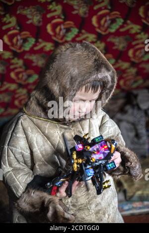 Un jeune Nenet jouant avec un jouet à l'intérieur d'un chum (tente traditionnelle couverte de peaux de rennes), Yamalo-Nenets Autonomous Okrug, Russie Banque D'Images