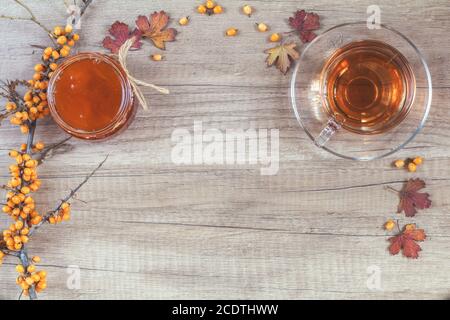 Concept de boisson chaude santé d'automne. Branche d'argousier commun avec baie, tasse de thé, jarre de confiture sur fond de bois clair. Banque D'Images
