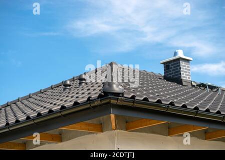 Le toit d'une maison unifamiliale recouverte d'un nouveau carrelage en céramique anthracite contre le ciel bleu, d'un carreau de crête visible, d'une cheminée système et d'une v céramique Banque D'Images