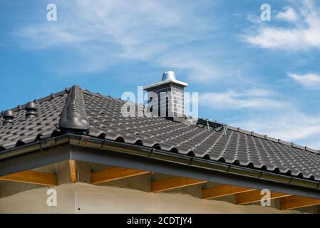 Le toit d'une maison unifamiliale recouverte d'un nouveau carrelage en céramique anthracite contre le ciel bleu, d'un carreau de crête visible, d'une cheminée système et d'une v céramique Banque D'Images