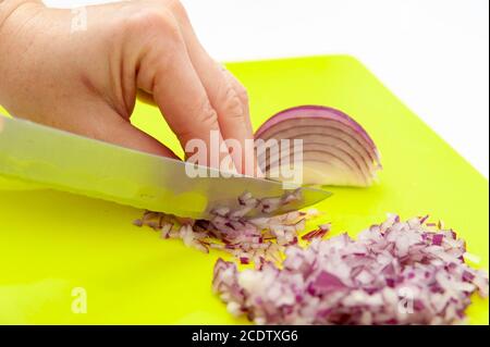 Les mains coupent l'oignon rouge pour préparer la vinaigrette brésilienne traditionnelle. Gros plan. Tir horizontal. Banque D'Images