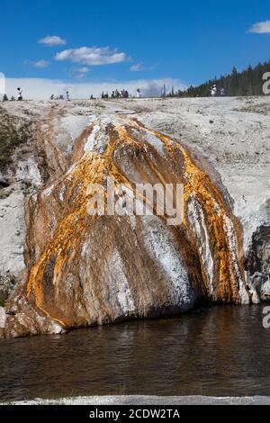 L'eau minérale chaude d'une source volcanique s'écoule vers le bas d'un remblai avec des bactéries orange créant des motifs sur la colline comme Il entre dans le Firehole RIV Banque D'Images