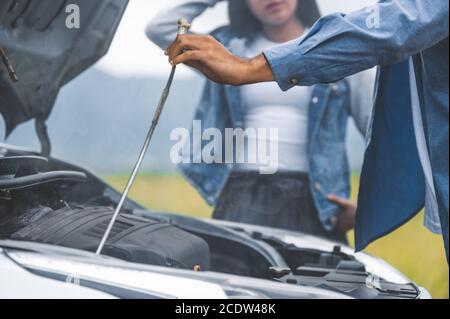 Homme asiatique ouvrir le capot de voiture pour la réparation comme service d'entretien avec le fond de femme entre le long voyage de route. Voiture cassée et panne dans la prairie de montagne wi Banque D'Images