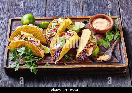 tacos de saumon avec salade de chou rouge déchiquetée et sauce au yaourt épicée parsemée de persil finement haché servi sur une planche sur une table en bois sombre, h Banque D'Images