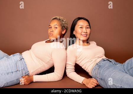 Deux jeunes femmes contemporaines de diverses ethnies qui se trouvent sur le sol Banque D'Images