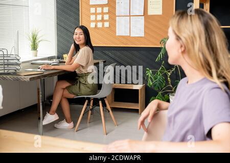 Femme asiatique souriante assise sur une chaise près d'un bureau et consultant avec un collègue Banque D'Images