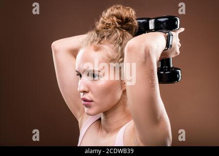 Active sweaty fille tenant des haltères dans les mains derrière la tête pendant exercice Banque D'Images