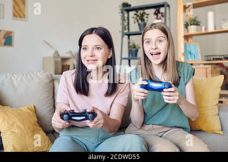 Adolescente excitée avec joystick assis sur le canapé à côté sa mère heureuse Banque D'Images