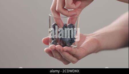 les mains de l'homme prennent les bleuets mûrs humides lavés du pot en verre sur fond neutre, photo large Banque D'Images