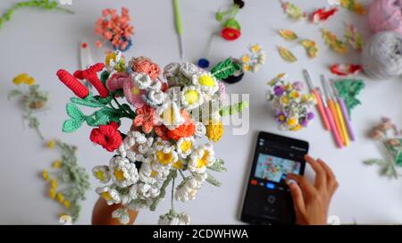 le temps de tournage fait main crochet produit de la photographe féminine, tenir à la main le bouquet de fleurs colorées comme rose, marguerite, feuille et prendre la photo par l'onglet sur blanc Banque D'Images