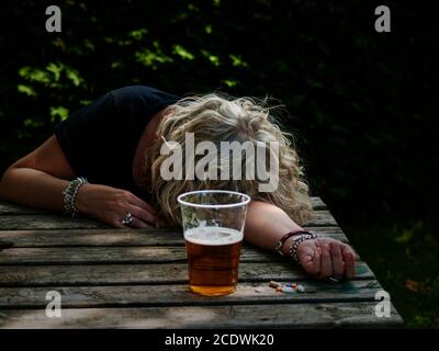 Une femme avec un grand nombre de pilules dans sa main de différentes couleurs et tailles et un verre de bière, Banque D'Images