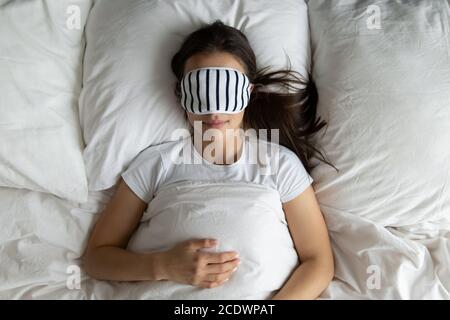 Vue de dessus paisible jeune femme portant un masque dormant dans le lit Banque D'Images
