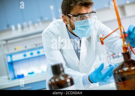 Beau chercheur en vêtements de travail de protection debout dans le laboratoire et flacon d'analyse avec liquide Banque D'Images