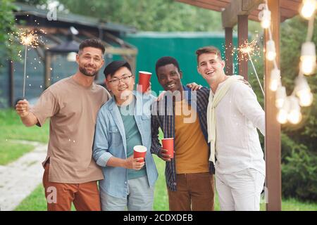 Groupe multi-ethnique d'amis masculins regardant l'appareil photo et tenant des spapers tout en appréciant la fête à l'extérieur, l'espace de copie Banque D'Images