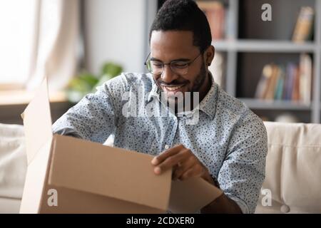 Souriant homme afro-américain portant des lunettes déballant le colis Banque D'Images