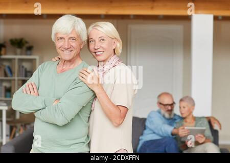Portrait d'un couple senior heureux souriant à l'appareil photo tout en étant debout dans la chambre avec un autre couple en arrière-plan Banque D'Images