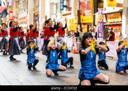 Équipe japonaise de femmes matures danseuses de yosakoi avec de petits enfants à l'avant, se concentrer sur la danseuse de jeunes filles s'agenouillant avec une écharpe jaune autour du poignet. Banque D'Images