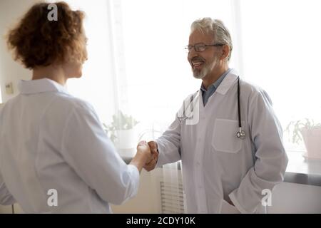 Sourire un médecin mature portant des lunettes saluant un collègue, en lui serrant la main Banque D'Images