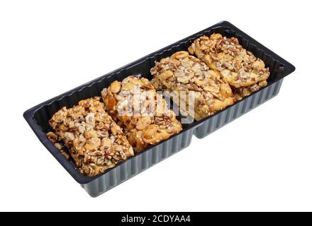 Biscuits carrés craquelins avec raisins secs, noix, arachides et graines dans boîte en plastique noir isolée Banque D'Images