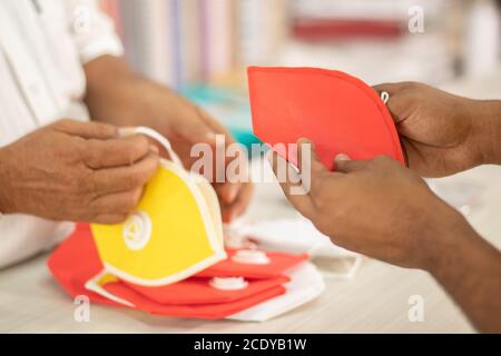 Accent sélectif sur le masque rouge, gros plan des mains de commerçant vendant des masques à l'acheteur pendant le coronavirus ou la pandémie Covid-19 - concept d'achat local ou Banque D'Images