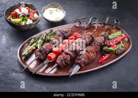 Shashlik russe traditionnel sur une brochette de barbecue avec salade de fermier et tzatziki comme un gros plan sur une planche à découper en bois Banque D'Images