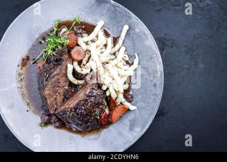 Joues de bœuf braisées allemandes traditionnelles dans une sauce au vin rouge brun avec des nouilles et des carottes offertes comme vue de dessus sur un design moderne p Banque D'Images
