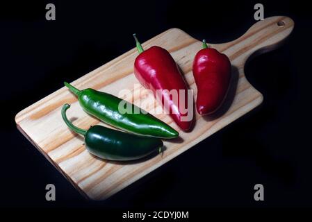 Assortiment de poivrons au Chili sur une planche à découper en bois rustique Sur fond noir Banque D'Images