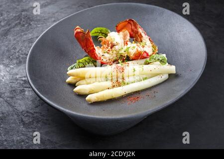 Queue de homard épicée traditionnelle au barbecue coupée en tranches et offerte en blanc asperges et laitue sur une assiette moderne Banque D'Images