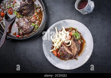 Joues de bœuf braisées allemandes traditionnelles dans une sauce au vin rouge brun avec des nouilles et des carottes offertes comme vue de dessus sur un design moderne p Banque D'Images