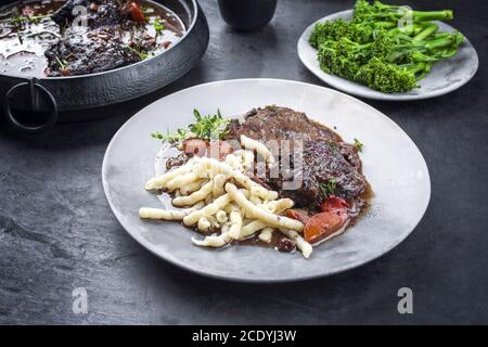 Joues de bœuf braisées allemandes traditionnelles dans une sauce au vin rouge brun avec nouilles et brocoli offert comme gros plan sur un moderne conception p Banque D'Images