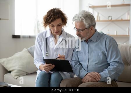 Jeune femme médecin infirmière consultant patient mature pendant la visite de soins à domicile Banque D'Images