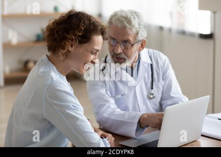 Sympathique médecin mature parlant au patient en train de rire lors de la réunion Banque D'Images