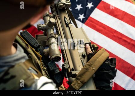 Gros plan d'un soldat américain portant son propre fusil au-dessus du drapeau national tout en se préparant au combat Banque D'Images