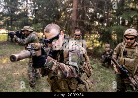 Des soldats armés ciblés en uniforme transportant des fusils et examinant la forêt terrain Banque D'Images