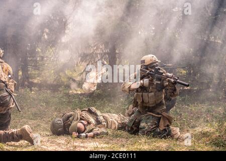 Soldat dans un casque debout sur les genoux près d'un collègue mort et en tirant sur le champ de bataille, brouillard dans la forêt Banque D'Images