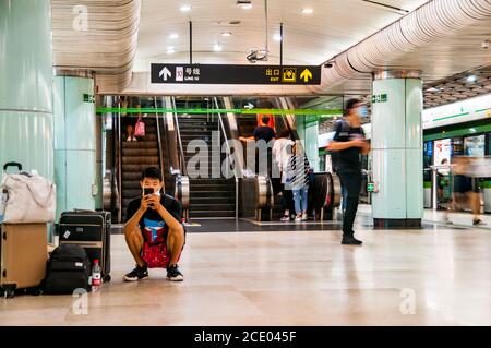 Un passager s'accrouille sur la plate-forme et utilise son téléphone en attendant un train à la gare est de Nanjing. Banque D'Images