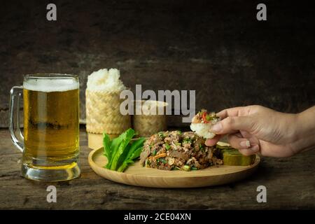 En utilisant une main pour manger du riz collant et de la salade de porc hachée épicée avec de la bière, Larb est la nourriture traditionnelle thaïlandaise est la culture de la population dans le nord-est de Banque D'Images