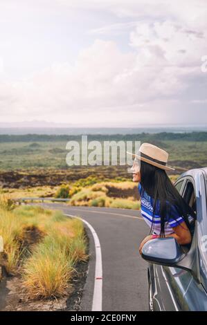 Une jeune femme portant un chapeau s'est penchée hors d'un fenêtre de voiture avec un beau paysage en arrière-plan Banque D'Images