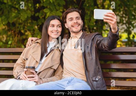 Couple amoureux de prendre selfie, assis sur banc dans le parc Banque D'Images