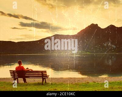 Effet de film. Seul l'homme est assis sur un banc à côté d'un lac de montagne azur. L'homme se détendre et observer les hauts sommets des Alpes au-dessus du lac M. Banque D'Images