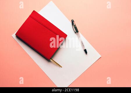 Carnet rouge couverture feuille blanche sur fond rose style pastel avec mise à plat de l'espace de copie Banque D'Images