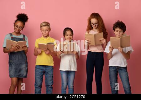 Des élèves diligents de différentes races lisant des livres ensemble sur le rose arrière-plan Banque D'Images