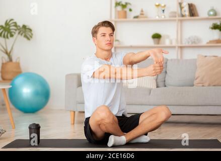Homme attrayant qui s'étire pour les exercices à la main sur le tapis Banque D'Images