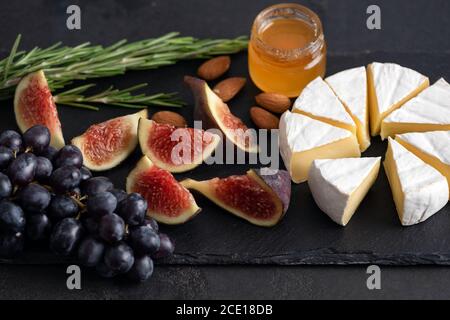 Fromage Camembert aux figues, raisins et miel. Plateau de fromages sur ardoise noire Banque D'Images