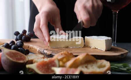 Préparation d'une assiette de fromages avec du fromage camembert doux, des figues et des raisins. Les mains de femme trancheuse le fromage Banque D'Images