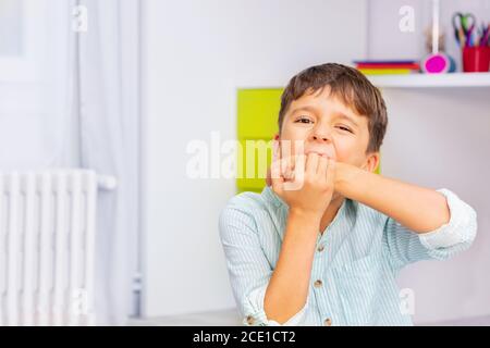 Portrait rapproché de petit garçon autiste mordant les mains avec une forte expression négative du visage assis dans sa chambre, problème d'auto-blessure Banque D'Images