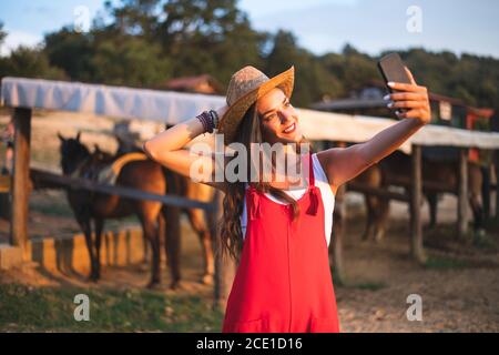 Souriante belle jeune femme appréciant sur la campagne à la ferme équestre et faire Selfie. Ranch concept Photographie Banque D'Images